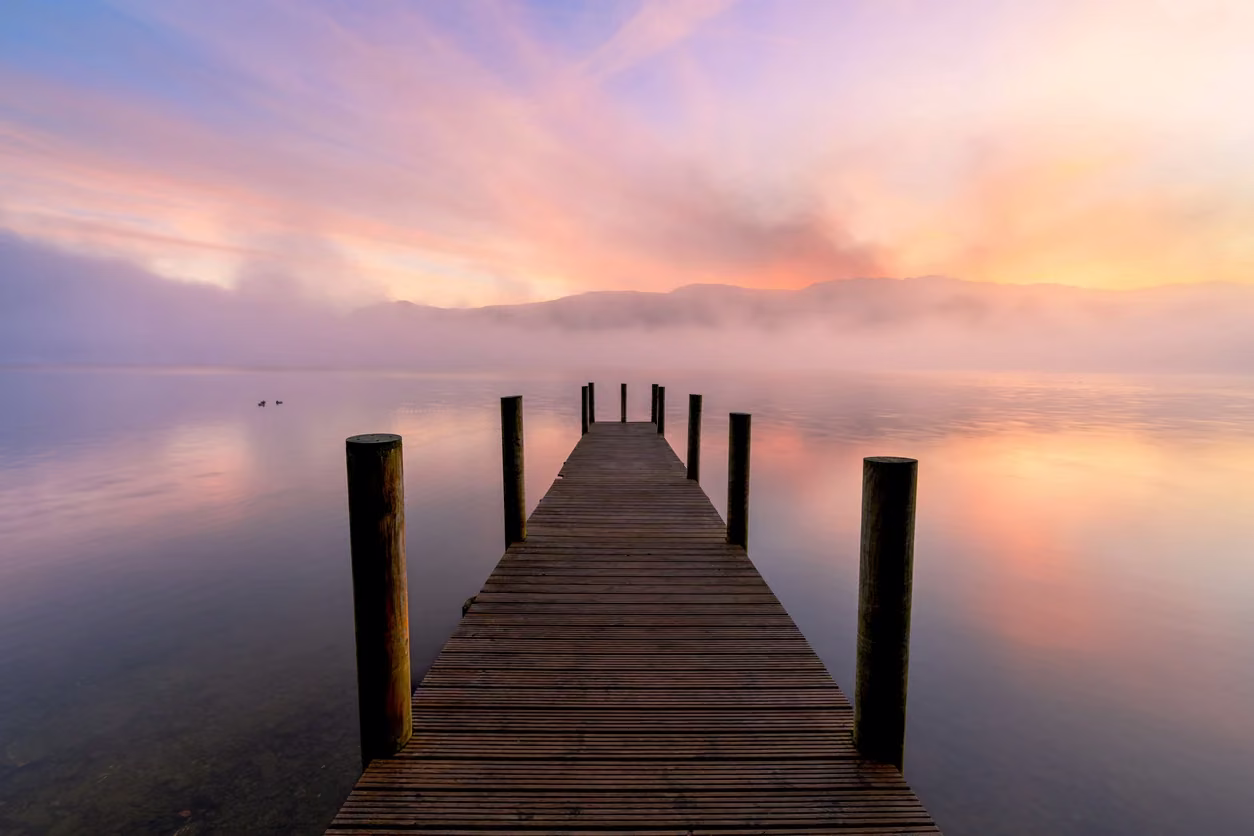 A quiet wooden dock extending into still water beneath a pink sky.